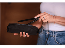 Charger l&#39;image dans la galerie, Femme tenant un lisseur noir et une pochette noire. Portant un haut blanc et un jean.
