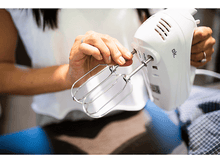 Charger l&#39;image dans la galerie, Une personne insère un accessoire de mixeur dans un batteur à main blanc. Le mixeur est sur une table.
