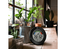 Charger l'image dans la galerie, Thermomètre sur une table en bois près de plantes près d'une fenêtre. Affiche la température et l'humidité.

