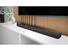 Charger l&#39;image dans la galerie, Une barre de son noire posée sur une surface blanche avec une TV.
