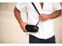 Charger l&#39;image dans la galerie, Un homme en chemise blanche tient une enceinte portable noire avec une sangle sur l&#39;épaule.
