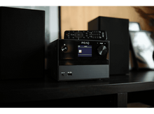 Charger l&#39;image dans la galerie, Chaîne stéréo noire sur une table sombre, avec enceintes et télécommande.
