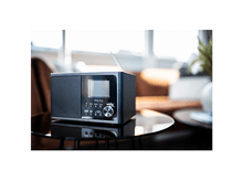 Charger l&#39;image dans la galerie, Radio noire avec affichage numérique sur une table en verre. Arrière-plan flou montre une pièce.
