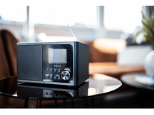 Charger l&#39;image dans la galerie, Radio noire sur une table en verre. La radio a un écran, des boutons et un bouton rotatif argenté.
