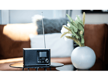 Charger l&#39;image dans la galerie, Une radio noire sur une table en verre avec un vase blanc et des fleurs.
