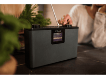 Charger l&#39;image dans la galerie, Une personne touche une radio noire et grise avec un petit écran.
