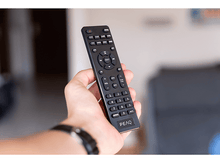 Charger l&#39;image dans la galerie, Main tenant une télécommande noire avec divers boutons, fond flou, design moderne.
