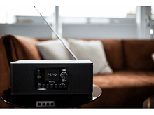 Charger l&#39;image dans la galerie, Radio PEAQ noire sur une table avec un canapé en arrière-plan. La radio a un écran.
