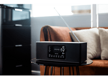 Charger l&#39;image dans la galerie, Radio PEAQ noire sur une table avec un canapé marron en arrière-plan.
