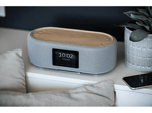 Charger l&#39;image dans la galerie, Haut-parleur gris avec un dessus en bois. Un écran affiche l&#39;heure. Une plante et un téléphone sont à côté.
