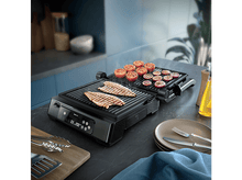 Charger l&#39;image dans la galerie, Gril avec tomates, oignons grillés et deux poissons. Gril noir avec pinces en métal. Fond de cuisine.
