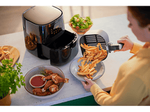 Charger l&#39;image dans la galerie, Friteuse à air avec des frites versées sur une assiette. Poulet et salade à proximité. Une personne tient.
