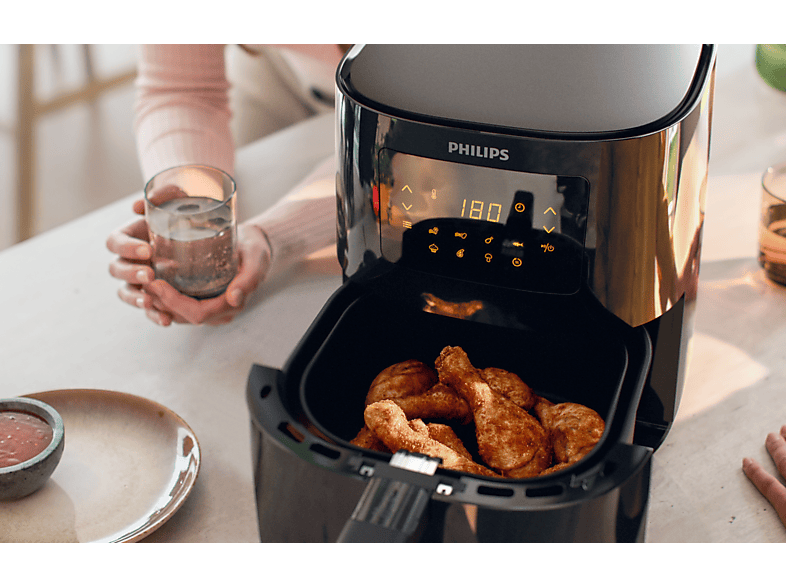 Friteuse à air avec poulet frit et une main tenant un verre d'eau.