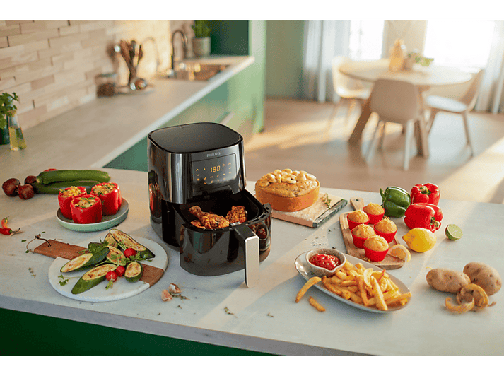 Un airfryer avec du poulet, divers aliments et ingrédients comme des poivrons, des courgettes et des pommes de terre.