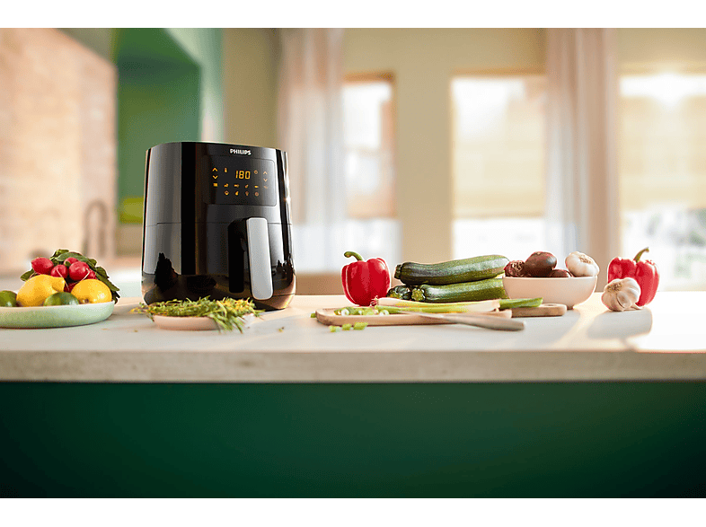 Friteuse à air Philips noire, avec légumes et aliments sur un comptoir.