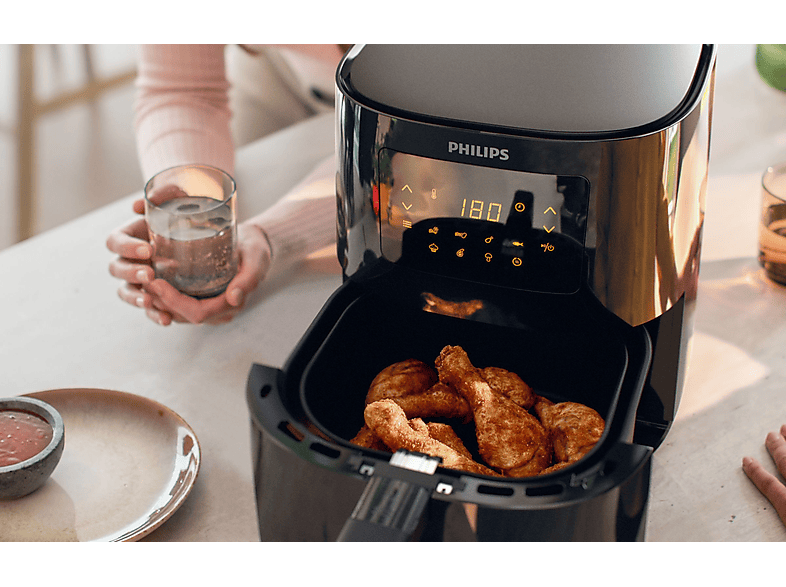 Friteuse à air avec des pilons de poulet frits dans le panier, personne tenant un verre.
