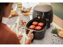 Charger l&#39;image dans la galerie, Femme près d&#39;une friteuse à air noire. Poivrons rouges dans le récipient. Cadre de cuisine.
