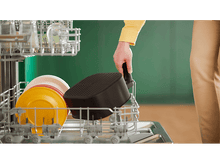 Charger l&#39;image dans la galerie, Une personne retire un panier de friteuse à air noir du lave-vaisselle. Assiettes et verres sont visibles.
