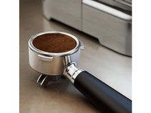 Charger l&#39;image dans la galerie, Gros plan sur un porte-filtre rempli de café moulu, près d&#39;une machine à café.
