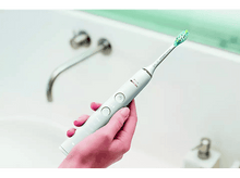 Charger l&#39;image dans la galerie, Brosse à dents électrique à la main, blanche. Arrière-plan de salle de bain.
