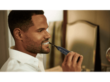 Charger l&#39;image dans la galerie, Un homme se brossant les dents avec une brosse à dents Philips Sonicare bleu foncé devant un miroir.
