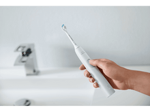 Charger l&#39;image dans la galerie, Main tenant une brosse à dents électrique blanche près d&#39;un lavabo et d&#39;un robinet.
