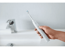 Charger l&#39;image dans la galerie, Une main tenant une brosse à dents électrique blanche près d&#39;un évier.
