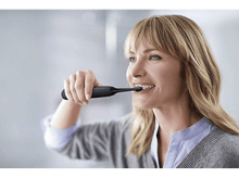 Charger l&#39;image dans la galerie, Une femme se brossant les dents avec une brosse électrique.
