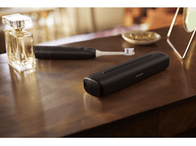 Charger l&#39;image dans la galerie, Une brosse à dents noire, un flacon de parfum et un plateau avec des bijoux sur une table en bois.
