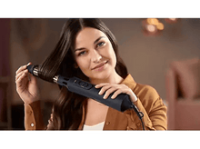 Charger l&#39;image dans la galerie, Une femme utilise un sèche-cheveux noir, coiffant ses cheveux, avec un arrière-plan doux.
