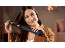 Charger l&#39;image dans la galerie, Femme tenant un styler à cheveux noir, souriante, chemise marron. Fond doux.
