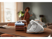 Charger l'image dans la galerie, Un fer à repasser à vapeur avec du linge sur une table et une femme en arrière-plan.
