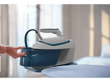 Charger l&#39;image dans la galerie, Main de femme ajoutant de l&#39;eau à un fer à repasser blanc et bleu, planche à repasser en arrière-plan.
