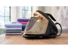 Charger l&#39;image dans la galerie, Fer à vapeur noir et doré sur une table en bois, avec des chemises pliées en arrière-plan.
