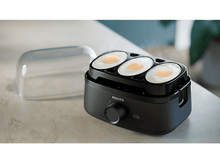 Charger l&#39;image dans la galerie, Cuiseur à œufs noir avec trois œufs à l&#39;intérieur, avec un couvercle transparent. Le cadran est à l&#39;avant.
