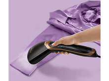 Charger l&#39;image dans la galerie, Une main qui repasse une chemise violette avec un défroisseur Philips noir et or.
