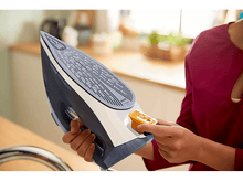 Charger l&#39;image dans la galerie, Personne repassant avec un fer blanc et bleu. Le fer est utilisé sur une surface en bois.
