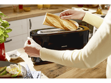 Charger l&#39;image dans la galerie, Une personne insère du pain dans un grille-pain Philips noir.
