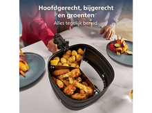 Charger l&#39;image dans la galerie, Une friteuse à air avec des ailes de poulet, des pommes de terre et des légumes. Des assiettes avec des légumes grillés sur les côtés. Des personnes en arrière-plan.
