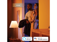 Charger l&#39;image dans la galerie, Un couple regarde à travers une porte, avec une lampe et le texte : Fonctionne avec Alexa, Google Assistant.
