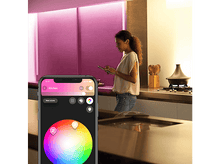 Charger l'image dans la galerie, Une femme utilise une tablette dans une cuisine moderne avec des lumières colorées. L'application sur le téléphone montre des options de couleur.
