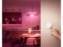 Charger l&#39;image dans la galerie, Une main touchant un interrupteur, avec une pièce éclairée en arrière-plan.
