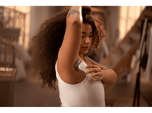 Charger l&#39;image dans la galerie, Une femme utilise un épilateur sur son aisselle, avec un arrière-plan clair.
