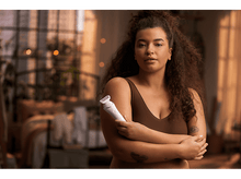 Charger l&#39;image dans la galerie, Une femme aux cheveux bouclés tient un épilateur blanc et rose. Elle porte un haut marron.
