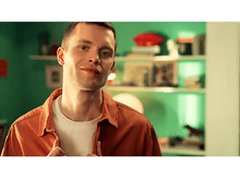 Charger l'image dans la galerie, Un homme en chemise orange et t-shirt blanc, souriant. Il est devant un mur vert.
