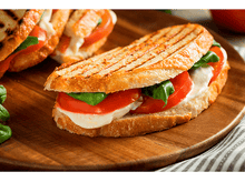 Charger l&#39;image dans la galerie, Un sandwich à la mozzarella, à la tomate et au basilic sur une planche en bois.
