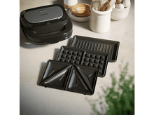 Charger l&#39;image dans la galerie, Un appareil à sandwich noir avec des plaques interchangeables sur une surface blanche. Comprend des plaques à gaufres.
