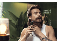 Charger l&#39;image dans la galerie, Un homme se rase le cou avec un rasoir noir et vert. Il a une moustache, un tatouage et porte un débardeur blanc.
