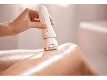 Charger l'image dans la galerie, Une main tenant un appareil blanc sur une jambe, appliquant une lotion, dans une salle de bain.
