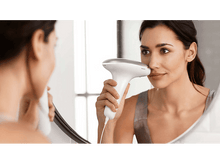 Charger l&#39;image dans la galerie, Une femme se regardant dans un miroir en utilisant un appareil d&#39;épilation faciale sur son visage.
